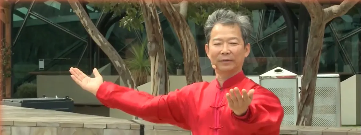 Master Han Jin Song demonstrating a Tai Chi form outdoors, arms open at shoulder level
