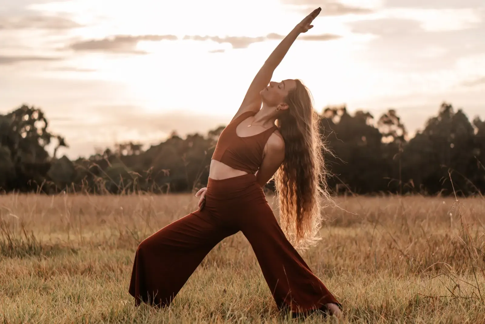 Indra-Kaye Staunton in a reverse warrior pose in a grassy field at sunset